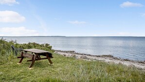 Ein Picknicktisch auf einer Wiese an einem ruhigen Gewässer unter blauem Himmel.