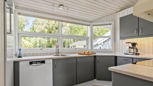 Eine moderne Küche mit grauen Schränken, einem Geschirrspüler und einem großen Fenster mit Blick auf Grünfläche.