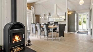 Ein modernes Interieur mit Kaminofen, Essbereich mit Stühlen und Tisch sowie Blick ins Freie durch eine Tür.