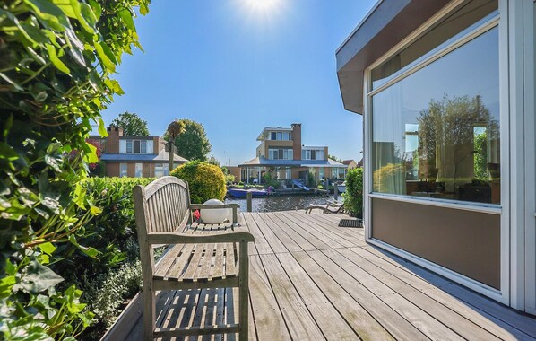 A wooden deck with a chair and a table, a glass door, and a view of a modern house across a body of water. - 2 bedroom gorgeous home in Lemmer (Lemmer)
