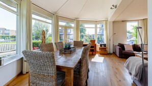 Ein geräumiger Raum mit einem Holztisch, Korbstühlen, einer Couch und großen Fenstern mit Blick nach draußen.