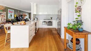 A modern kitchen with white cabinets, a central island, and a dining area with wooden chairs. - Spacious Bayside Elwood Home. Walk to the beach, the botanical gardens, cafes.. (Elwood)