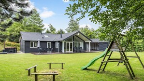 Ein modernes Haus mit Terrasse, einer grünen Rutsche und einer hölzernen Schaukel.