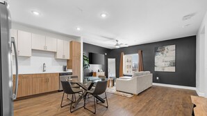 A modern kitchen with white cabinets, a dining area with a glass table, and a living room with a white sofa. - The Hidden Hills Suite The Gulch (Nashville)