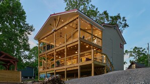 A multi-story wooden building with balconies and string lights, surrounded by trees. - Freshly Remodeled House! Overlooks Dale Hollow! (Byrdstown)