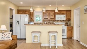 A kitchen with wooden cabinets, a central island with stools, a refrigerator, a microwave, and pendant lights. - Freshly Remodeled House! Overlooks Dale Hollow! (Byrdstown)