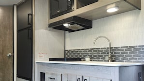A modern kitchen with built-in appliances, a stainless steel sink, and a backsplash with hexagonal tiles. - Cozy RV Vacation (Antioch)