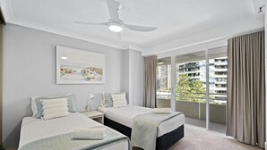 A hotel room with two beds, a ceiling fan, a large window with curtains, and a city view.