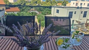 A balcony with a view of buildings, a potted lavender plant, and two drinks with garnishes. - Awesome apartment in Brodarica with sauna (Brodarica)