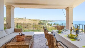 A balcony with wicker furniture, a table set for dining, and a view of the sea and hills. - Stunning home in Ciotta with WiFi (Ciotta)