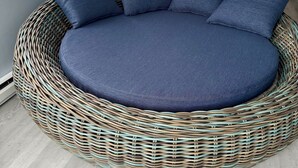 A round wicker sofa with a dark blue cushion and matching pillows, set against a light-colored wall and wooden floor. - Stylish Seaside Serenity with Pool Jersey Shore - Heart-Shaped Tub & Sunroom (Seaside Heights)