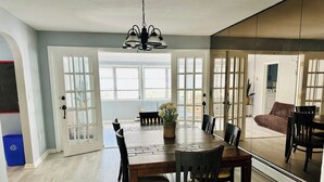 A dining area with a wooden table and chairs, large windows, and a chandelier. - Stylish Seaside Serenity with Pool Jersey Shore - Heart-Shaped Tub & Sunroom (Seaside Heights)