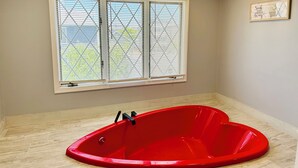 A bathroom with a red bathtub, a window with blinds, and a framed quote on the wall. - Stylish Seaside Serenity with Pool Jersey Shore - Heart-Shaped Tub & Sunroom (Seaside Heights)