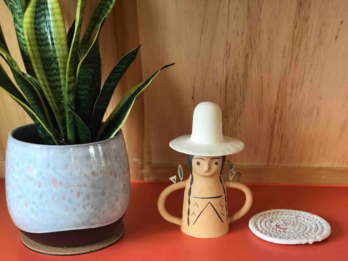 Una maceta con una planta, una figurita de cerámica con sombrero y un felpudo enrollado sobre una superficie de madera.