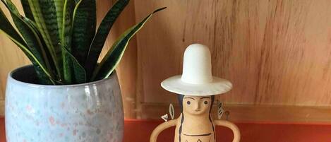 Una maceta con una planta, una figurita de cerámica con sombrero y un felpudo enrollado sobre una superficie de madera.