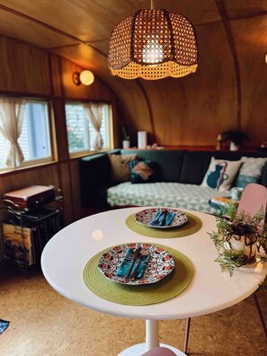 Ein Esstisch mit Tellern und Besteck, eine Hängelampe und ein Bett mit Kissen in einem Zimmer mit Holzwänden.