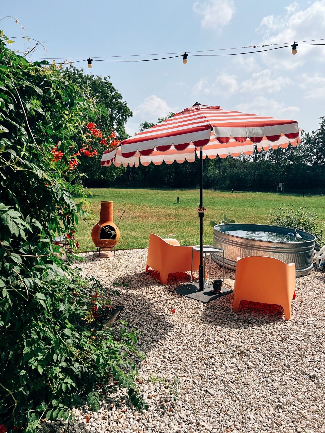 A patio area with a striped umbrella, outdoor seating, a fire pit, and a hot tub.