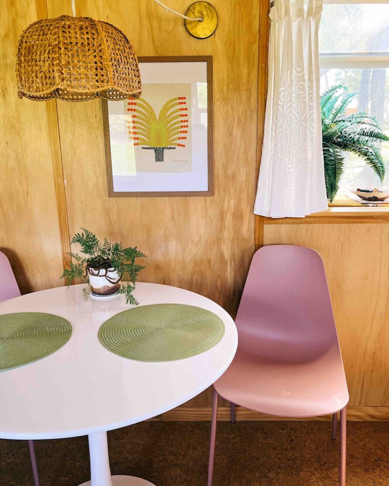Un comedor con una mesa redonda, dos sillas, una lámpara colgante, un cuadro enmarcado y una ventana con cortinas.