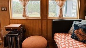 Una habitación acogedora con cama, un taburete pequeño y redondo, una maleta y una estantería con libros.