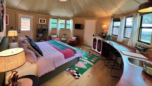A cozy bedroom with a large bed, a small desk, and a kitchenette. - Silo house - 3 acres +pool +outdoor shower  “Opal” (Austin)