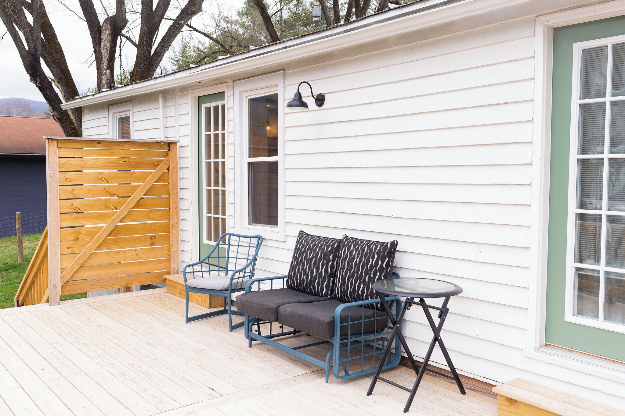 A covered patio with a sofa and chairs, a small table, and a wooden gate.