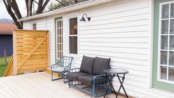 A covered patio with a sofa and chairs, a small table, and a wooden gate.