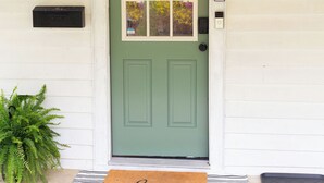 A green door with a window, a mailbox, a welcome mat, and a potted plant.