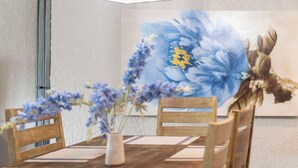 Un coin repas avec une table en bois, des chaises, un vase de fleurs et un grand tableau floral accroché au mur.