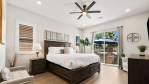 Ein Schlafzimmer mit einem großen Bett, einem Deckenventilator, einem Nachttisch, einer Lampe und Blick auf die Außenpatio.