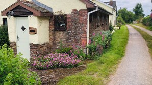 Une maison de campagne à l’aspect rustique, avec une porte blanche, des murs en pierre et un chemin de gravier menant à l’entrée.