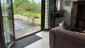 Une pièce dotée d’une porte-fenêtre coulissante donnant sur un jardin, d’une cheminée en pierre et d’un coin salon confortable.