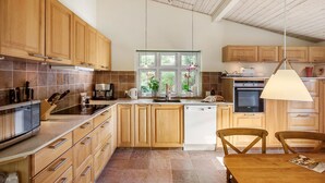 A modern kitchen with wooden cabinets, a built-in oven, a coffee maker, and a window with plants. - Pet friendly home in Stege with WiFi (Stege)