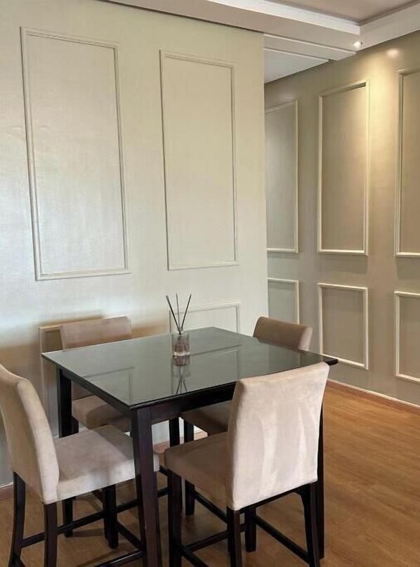 A dining area with a glass table and four chairs, a vase with a candle, and a wall with paneling.