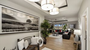 A modern living room with a large black and white landscape painting, a wooden bench with white cushions, a deer sculpture, and a large potted plant. - Elegant + Modern Home + Patio (Waukee)