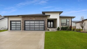 A modern two-story house with a stone facade, two garage doors, and a well-maintained lawn. - Elegant + Modern Home + Patio (Waukee)