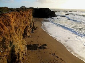 A coastal beach with a cliff, waves, and a distant structure. - Belle Maison D'architecte Pour 8/10 Personnes Proche de la Plage et Côte Sauvage (Piriac-sur-Mer)