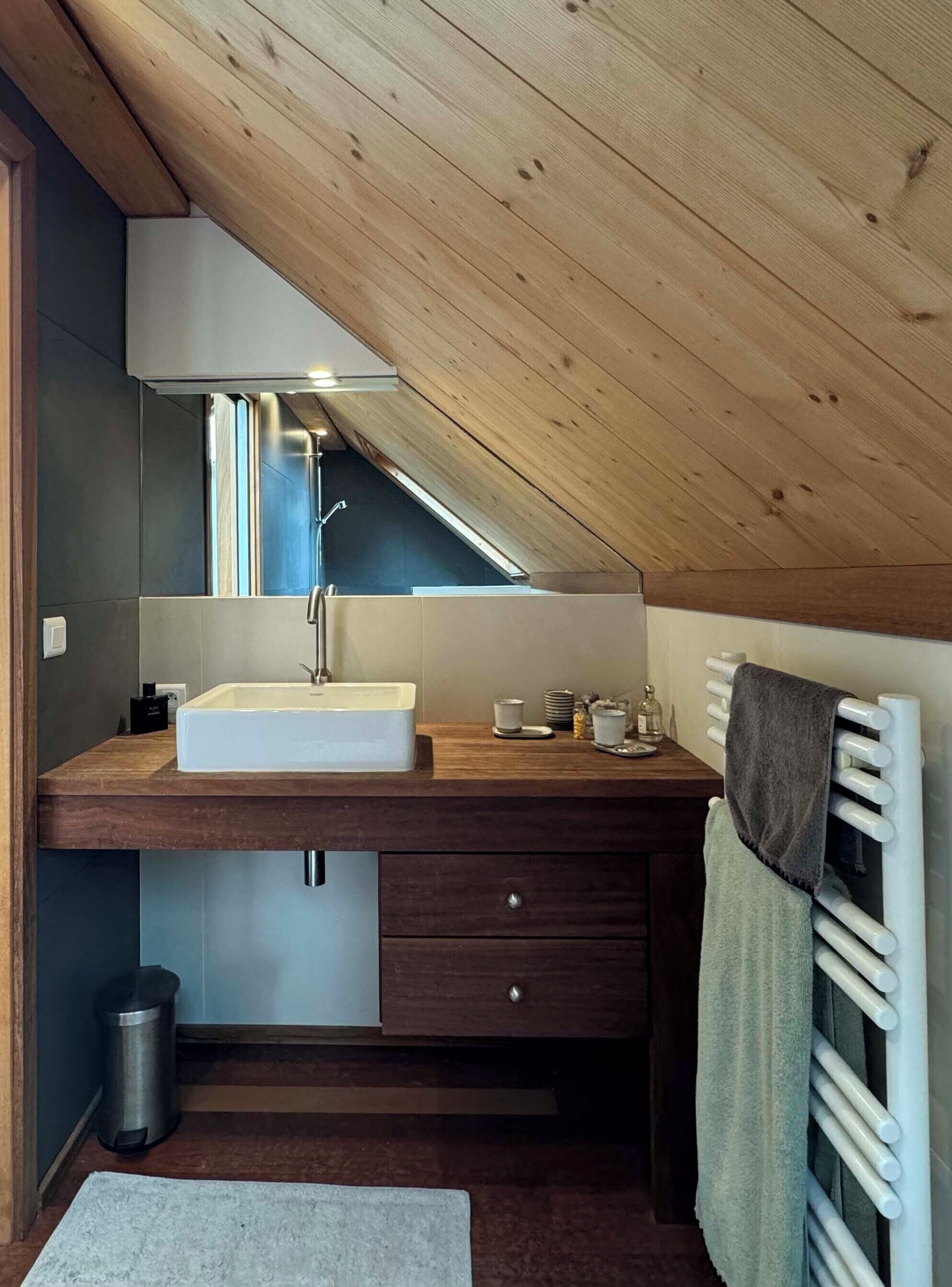 A modern bathroom with a wooden ceiling, a white sink, a mirror, and a towel rack.