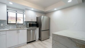 A modern kitchen with white cabinets, stainless steel appliances, and a marble countertop.