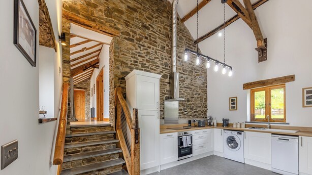 A kitchen with a stone wall, wooden staircase, and modern appliances. - 2 bedroom accommodation in Southgate, near Aberystwyth (Southgate, near Aberystwyth)