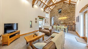 A spacious living room with a stone wall, wooden beams, a television, and a dining area. - 2 bedroom accommodation in Southgate, near Aberystwyth (Southgate, near Aberystwyth)