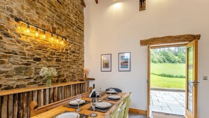 A dining area with a stone wall, wooden table, and chairs. There are framed pictures on the wall and a door leading outside. - 2 bedroom accommodation in Southgate, near Aberystwyth (Southgate, near Aberystwyth)