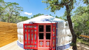 Uma yurta tradicional com exterior vermelho e branco, localizada em um deck de madeira rodeado por árvores.