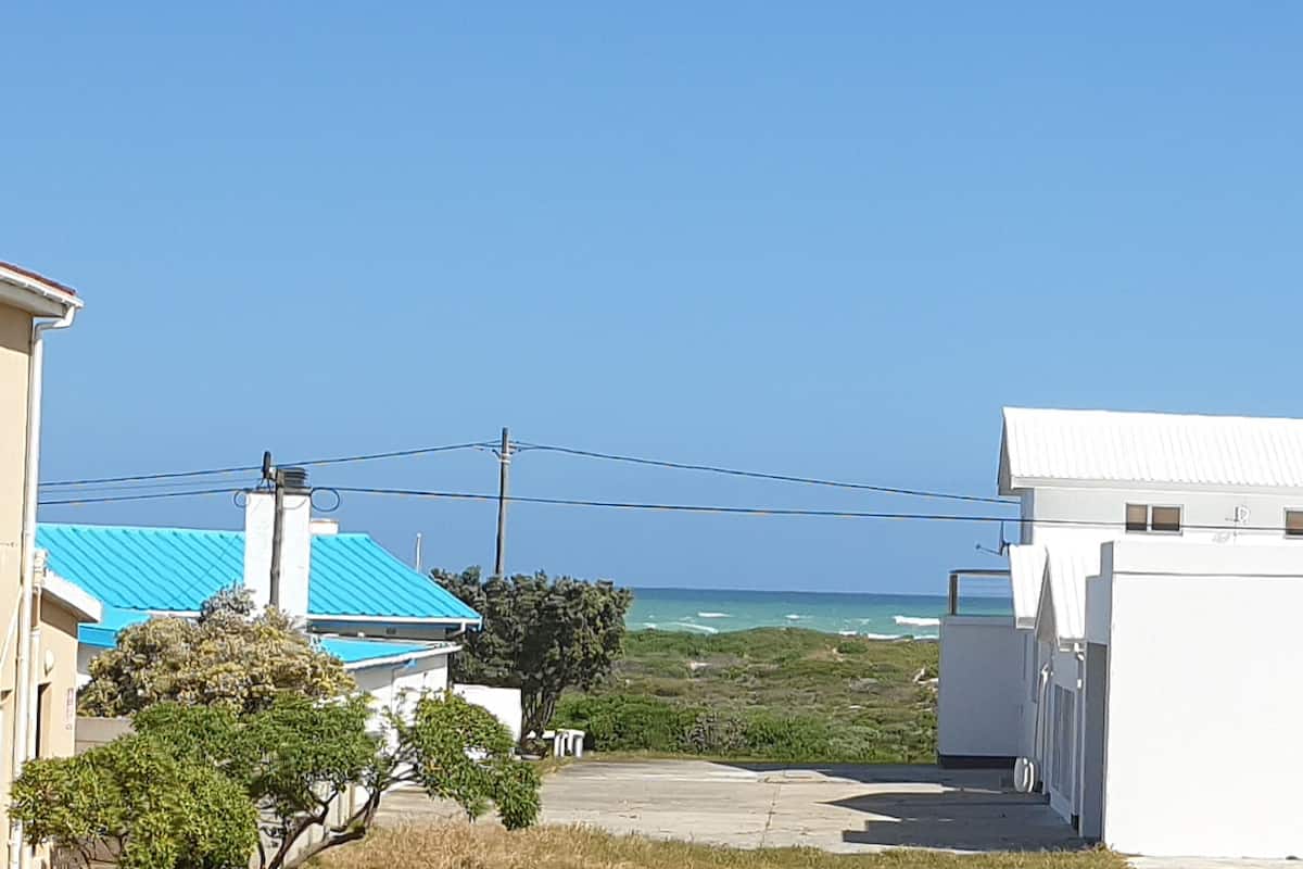 A coastal residential area with houses, a clear sky, and the ocean in the background.
