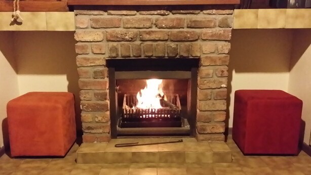 Une cheminée avec un manteau en briques, un feu qui crépite à l’intérieur, et deux bancs rouges rembourrés de chaque côté.