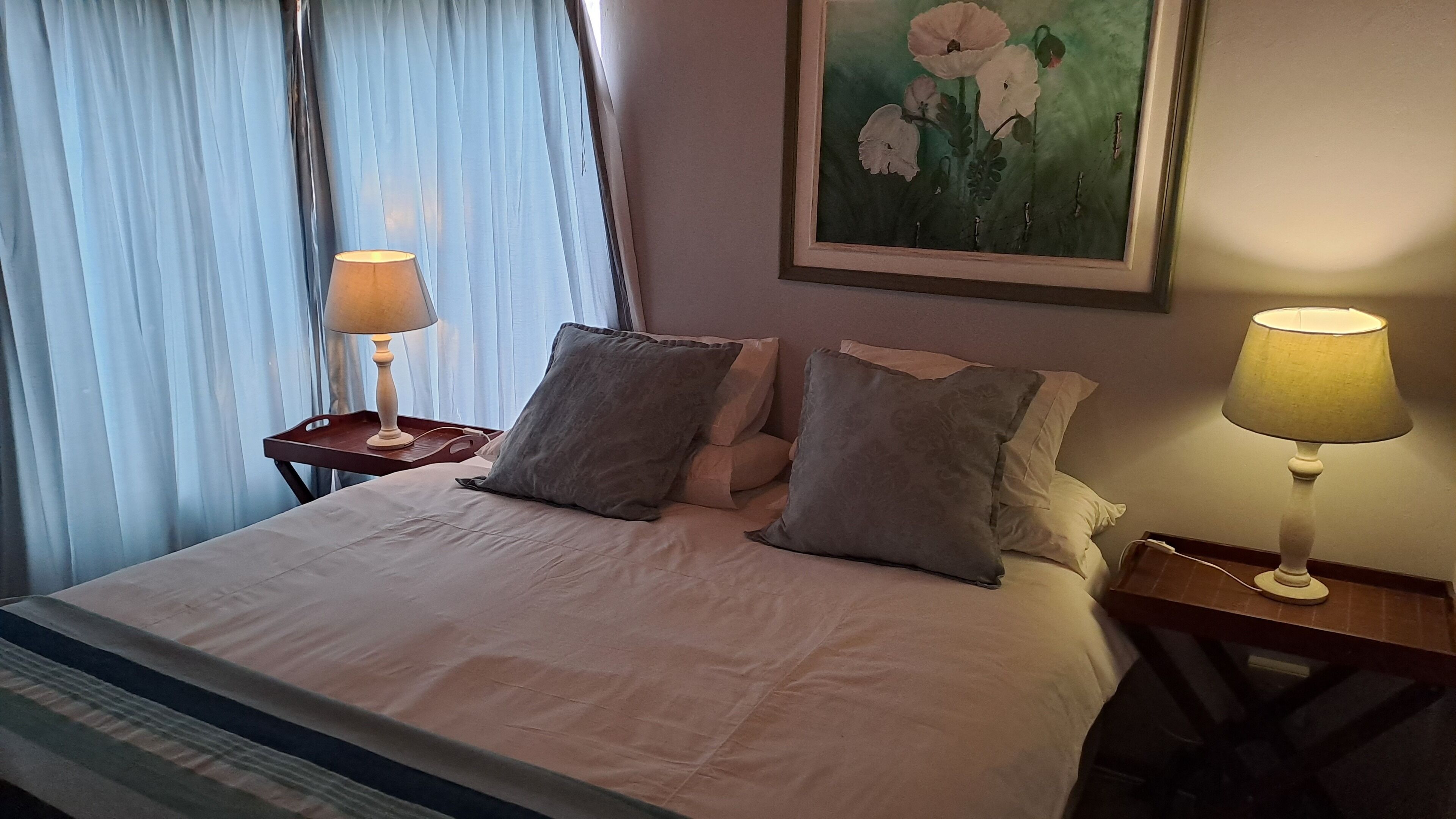 A hotel room with a large bed, two bedside tables with lamps, a painting on the wall, and a window with curtains.