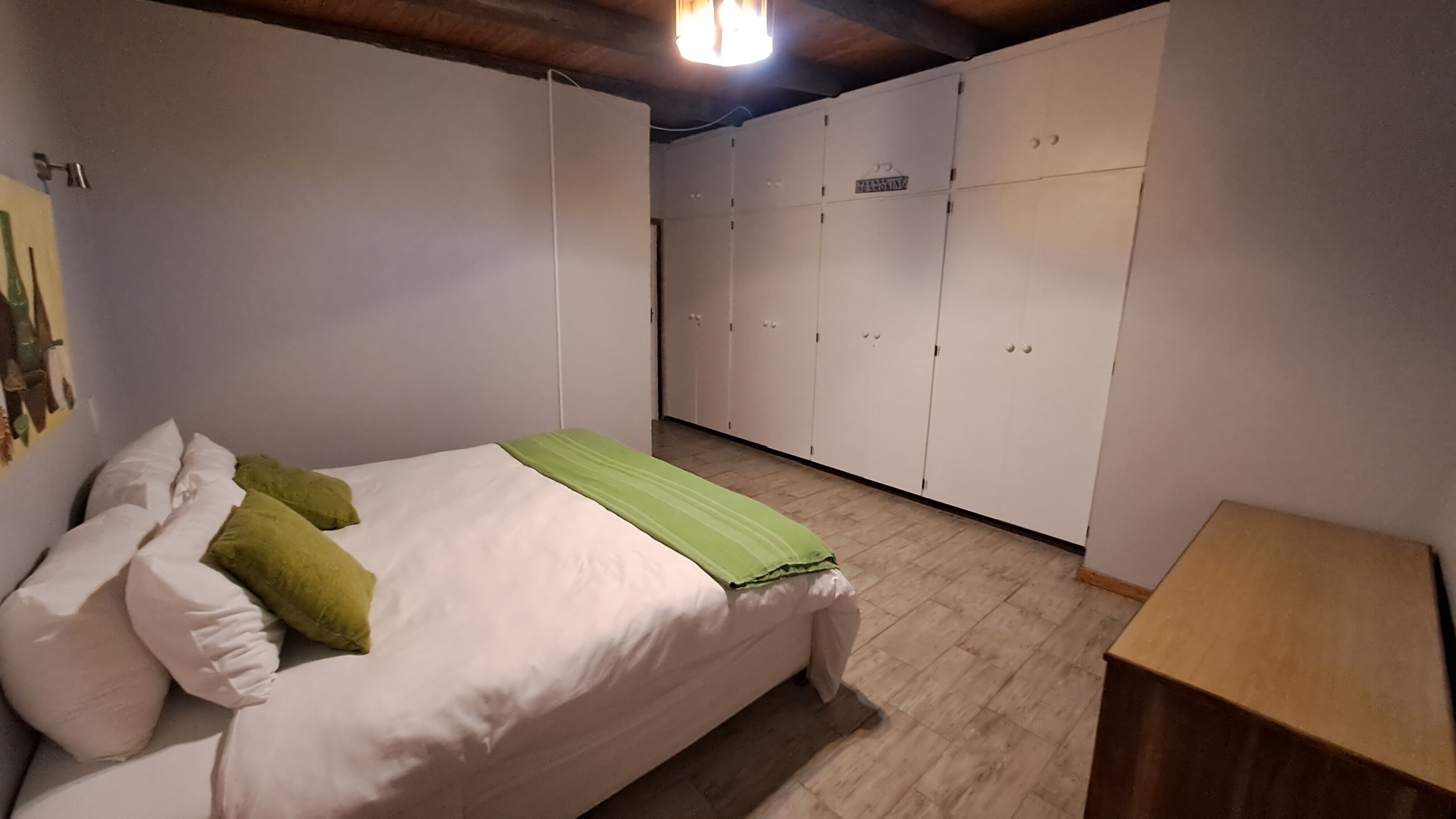 A bedroom with a bed, green and white pillows, a wooden nightstand, and a wardrobe with multiple doors.