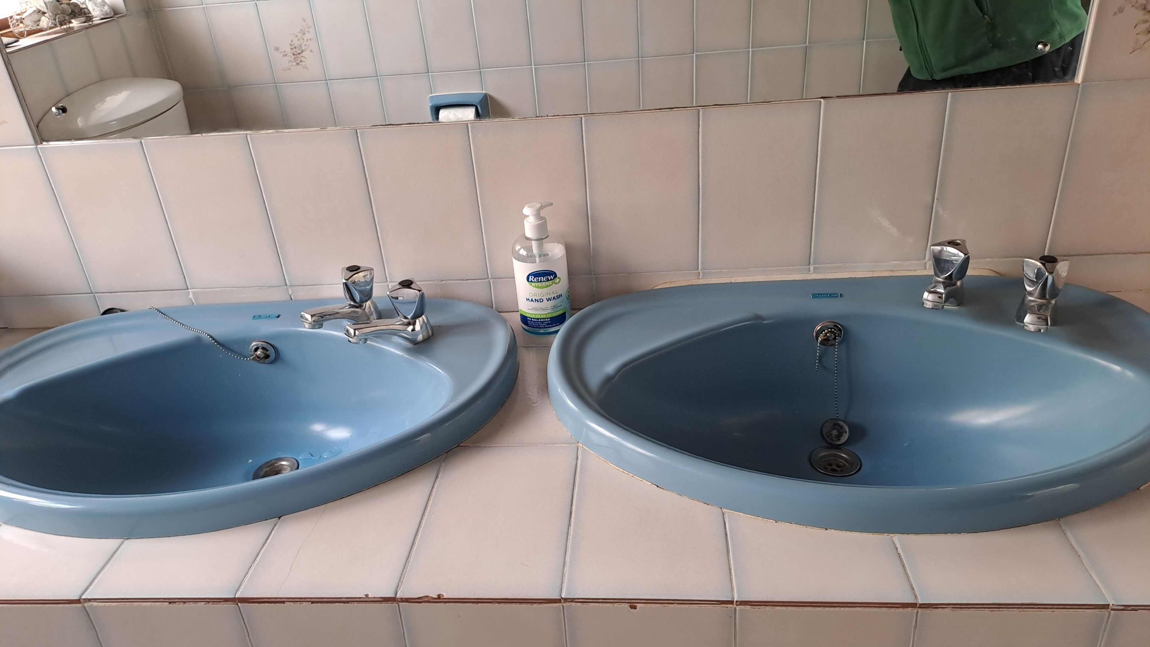 Un baño con dos lavamanos azules, un inodoro y una botella de gel hidroalcohólico.