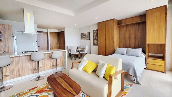 Ein modernes Hotelzimmer mit einem großen Bett, einer Couch, einem Holztisch, einer Küchenzeile und einem Esstisch.
