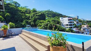 Ein Pool auf dem Dach mit Stufen, umgeben von Grünflächen und Gebäuden.