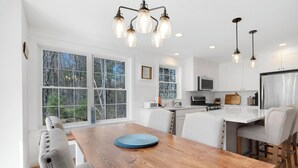 A modern kitchen with white cabinets, a wooden dining table, and pendant lighting. - Spacious Pet Friendly-Close to Beach and Town! (Kennebunk)